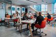 © qunica.com - A diverse group of professionals works in a bright, open-plan coworking space. People sit at white tables with laptops and coffee, collaborating in a modern office.