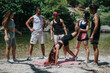 © qunica.com - Group of friends on a sunny riverside watch as a teammate does a handstand; others cheer and observe.