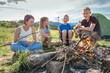 © Soloviova Liudmyla - Happy diverse group of children and teenagers roasting marshmallows on campfire during summer camping trip featuring green tent and mountain landscape background area for youth lifestyle concept