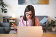 © Studio Marmellata - A woman wearing glasses and a pink blazer is actively engaged in a video call on her laptop, gesturing with her hands as she communicates.