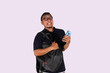 © Dyto - An adult Asian man wearing glasses stands with a cheerful expression while holding a cell phone and a bag. Advertising model concept