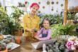 © sofiko14 - A woman and a young girl smile while working with plants, creating a heartwarming scene of family and nature