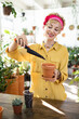 © sofiko14 - A smiling woman carefully tends to a plant, adding soil to a small pot with a trowel