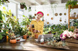 © sofiko14 - A woman is seen repotting a succulent plant while using a laptop in a bright greenhouse setting