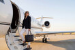 © Oleg Ivanov - Stylish woman boarding a private jet on the airport tarmac, luxury VIP charter travel and executive lifestyle concept with copy space, sunglasses and designer-style tote bag