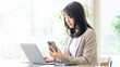 © Trickster* - スマートフォンを持ちながらノートパソコンを見る女性ビジネスパーソン, Businesswoman holding smartphone while looking at laptop