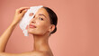 © Home-stock - Beautiful European lady removing moisturizing white fabric sheet mask from her face after using it, looking at camera, posing on pink background