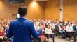 © tahir xh - A dynamic male speaker, viewed from behind, confidently addresses a substantial, diverse audience gathered within a well-lit conference hall during an engaging business seminar.