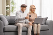 © Ljupco Smokovski - Mature man holding a credit card seated on a sofa next to a woman with a laptop