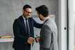 © Novak - Two professional businessmen in formal suits shaking hands in a modern office, sealing a deal, representing successful partnership, trust, and corporate agreement