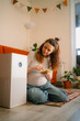 © wifesun - Pregnant woman sitting on the floor adjusting a smart air purifier using a mobile application on her smartphone, ensuring a healthy indoor environment for herself and her future baby