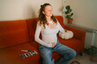 © wifesun - Pregnant woman seated on a couch meditating with hands on belly and chest, calm and focused amid sonogram prints and positive test, embracing prenatal self-care and quiet anticipation