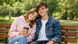 © Nataliia Pyzhova - Happy teenage couple sitting on park bench with coffee in summer sunshine. Young love and friendship outdoors.