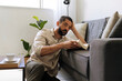 © kleberpicui - Adult man relaxing on sofa reading book at home with coffee nearby. Calm lifestyle moment representing mindfulness, rest and slow living in modern bright interior.