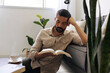 © kleberpicui - Adult man relaxing on sofa reading book at home with coffee nearby. Calm lifestyle moment representing mindfulness, rest and slow living in modern bright interior.