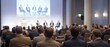 © JasmineStudio - A group of formally dressed people sitting in rows of chairs watching a panel discussion on a large screen in a conference room with a stage and a podium