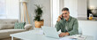 © insta_photos - Happy busy middle aged mature man senior entrepreneur talking on mobile phone looking at laptop using computer calling on cellphone working at home sitting at kitchen table.
