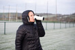 © Мар'ян Філь - Woman wearing a black jacket drinks from a white travel mug on frosty sports field, warming up between outdoor winter training or exercise sessions in cold weather