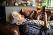 © Geber86 - Senior man using smartphone while lying on sofa at home