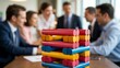 © Kage Dojo - A group of professionals are engaged in a meeting, with a colorful wooden block tower game in the foreground symbolizing teamwork and strategy.