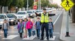 © Mohsin - Dedicated school crossing guard safely stops traffic with a stop sign allowing a group of diverse young students to cross the busy street on transparent background