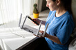 © kazakova0684 - Woman Setting Up White Wi-Fi 6 Router with Smartphone in Bright Sunny Home Office Interior
