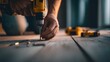 © arayabandit - A close up shot captures a person's hands using a yellow power drill to drive a screw into a wooden floor, highlighting construction and craftsmanship.