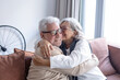 © luciano - Happy bonding elderly couple sitting on sofa in a modern home relaxing and embracing exchanging cuddles and kisses, enjoying carefree moments together in good mood and harmony