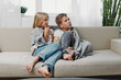 © SHOTPRIME STUDIO - Two children wrapped in a blanket sit barefoot on a modern sofa, looking engaged and cozy in a bright living room with natural plants in the background.