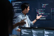 © SAT65 - Asian Male software engineer pointing at source code on a large screen during a tech team meeting, explaining Code on the Screen, Discussing on coding task, New software development project in office.