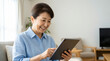 © M - Happy senior Japanese woman using a digital tablet in a sunlit living room with copy space