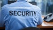 © dmmarychev - Back view of security guard in blue uniform sitting at desk in office
