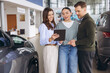 © anatoliycherkas - Saleswoman showing car options on tablet to a couple buying a new vehicle in an auto dealership showroom