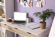© Pixel-Shot - Comfortable workplace with modern laptop and houseplant near violet wall in room, closeup