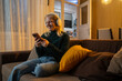© Nenad - Image of smiling nice woman using cellphone while sitting on sofa