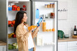 © Pixel-Shot - Young Asian woman with bottle of water and juice near open fridge in kitchen