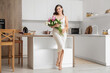 © Pixel-Shot - Beautiful young woman with bouquet of peony flowers in kitchen