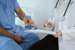 © Witoon - Doctor consulting with a patient in a clinic, reviewing medical documents on a clipboard while the patient points at the paperwork during a healthcare appointment.