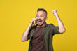 © ReyRomMedia - Attractive handsome 50s man over isolated yellow background have mobile conversation over smartphone in victory position. casual man hearing excelent news over phone and celebrating success with fire