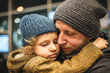 © Kowit - A tender moment between a father and child warmly embracing, both wearing knitted hats and cozy sweaters in an indoor setting.