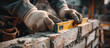 © Menganga - Construction worker's hands placing a brick on mortar, using a spirit level to ensure accuracy during modern wall building
