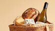© dinatychynska - Picnic basket filled with artisan bread, cheese varieties, wine bottle, striped cloth. Gourmet food selection, sustainable packaging, organic products, outdoor dining essentials, beige background.