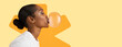 © Prostock-studio - A woman is blowing a bubble with gum. She faces sideways with a warm expression. The background has a bright yellow color with a playful design. The scene is lively and fun.