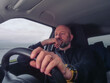 © mark_gusev - Bald male driver in his 40s or 50s in dark clothes. Man with grey beard behind driving wheel, Transport and tourism.