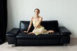 © Tanya Danilevich/Stocksy - A girl sitting on a black leather sofa.