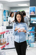 © DC Studio - Middle aged Asian woman reviews pharmaceutical product for heart recovery treatment. Confident female customer shops for prescription medicine and over the counter healthcare products in pharmacy.