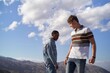 © Studio Sincère/Stocksy - Two men standing on a mountain peak with a blue sky