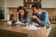 © Miljan Živković - Stressed young couple managing bills and financial problems at home