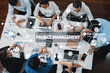 © InfiniteFlow - A top-down view of a diverse team participating in a project management meeting, highlighting resource planning and risk assessment through visual diagrams and charts. Amity