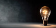 © Nguyen - Close Up of a Classic Glowing Incandescent Light Bulb on Dark Textured Surface Representing a Single Great Idea Innovation Invention and the Power of Bright Thinking in Darkness
